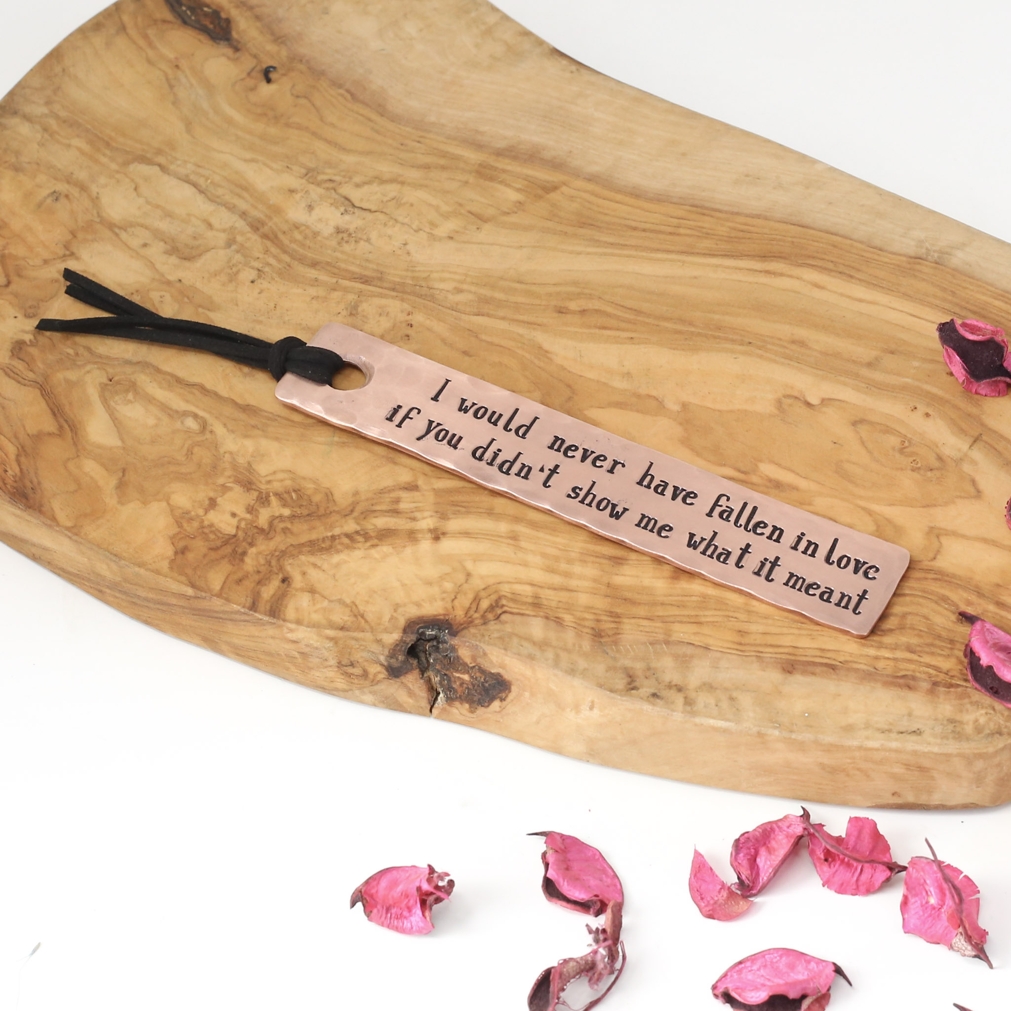 9th Anniversary Copper Bookmark. Pictured on a rustic wooden board, bookmark has been hand stamped with a personalisation and finished with a soft blk faux leather tassel